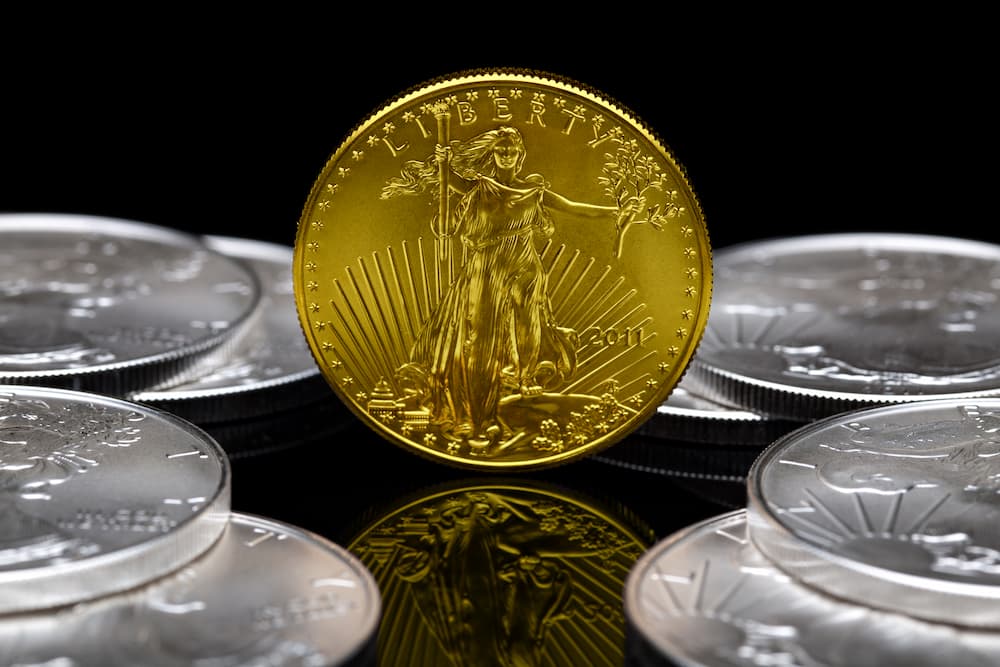 An american golden eagle bullion coin in the center and silver bullion coins laying around it. 